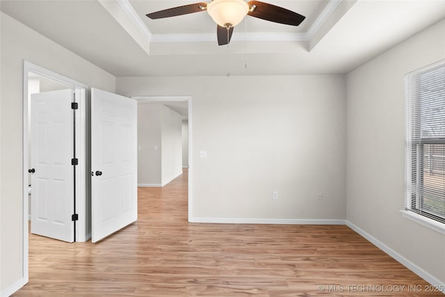 empty room with ornamental molding, a tray ceiling, baseboards, and light wood finished floors