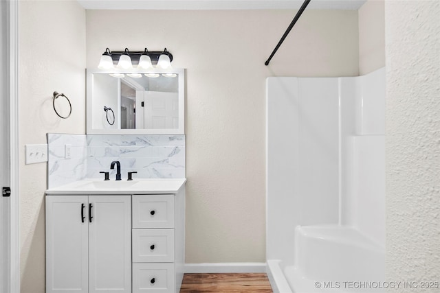 full bathroom featuring tasteful backsplash, walk in shower, wood finished floors, and vanity