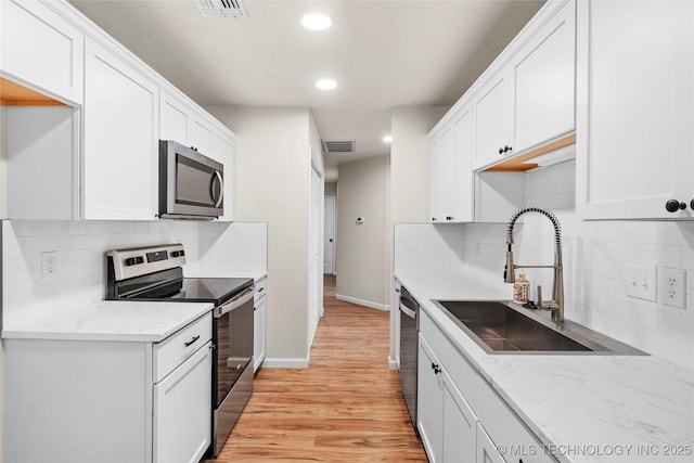 kitchen featuring stainless steel appliances, light wood-style flooring, a sink, and white cabinetry