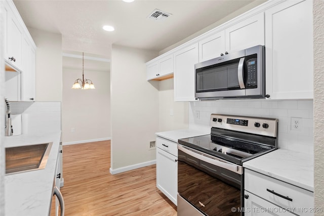 kitchen with light stone counters, visible vents, appliances with stainless steel finishes, light wood-style floors, and white cabinetry