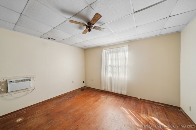 unfurnished room with visible vents, a drop ceiling, wood-type flooring, ceiling fan, and a wall mounted AC