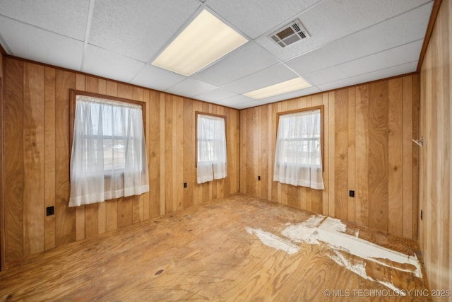 unfurnished room featuring visible vents, wooden walls, and a drop ceiling