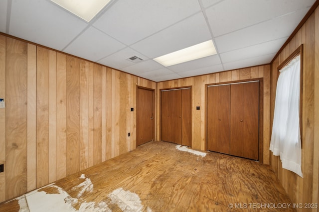 interior space featuring a paneled ceiling, two closets, visible vents, and wooden walls