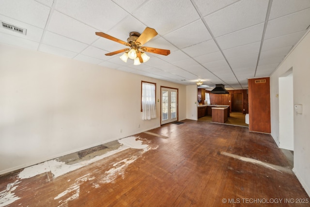 unfurnished living room featuring a paneled ceiling, dark wood-type flooring, visible vents, baseboards, and a ceiling fan