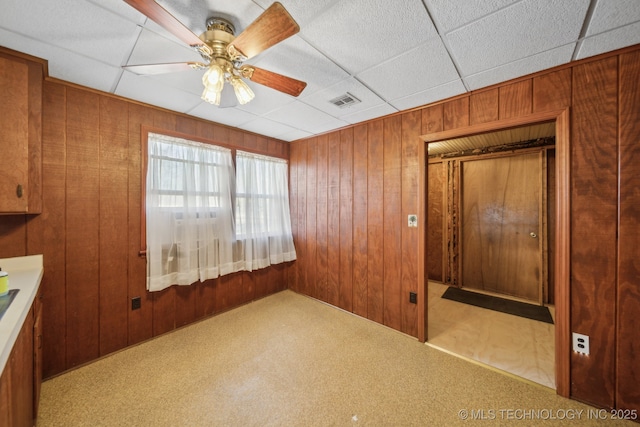 unfurnished bedroom with a paneled ceiling, visible vents, wooden walls, and carpet flooring