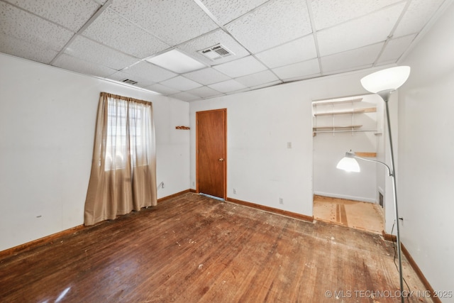 spare room with a paneled ceiling, wood-type flooring, visible vents, and baseboards