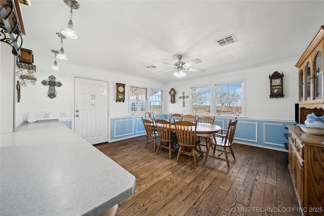 dining space with crown molding, visible vents, dark wood finished floors, a decorative wall, and a ceiling fan