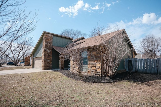 view of property exterior featuring driveway, stone siding, an attached garage, and fence