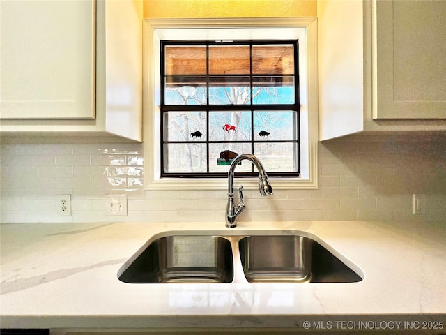 interior details featuring light stone counters, decorative backsplash, white cabinets, and a sink