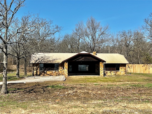 view of front of house featuring a chimney, fence, stone siding, and metal roof