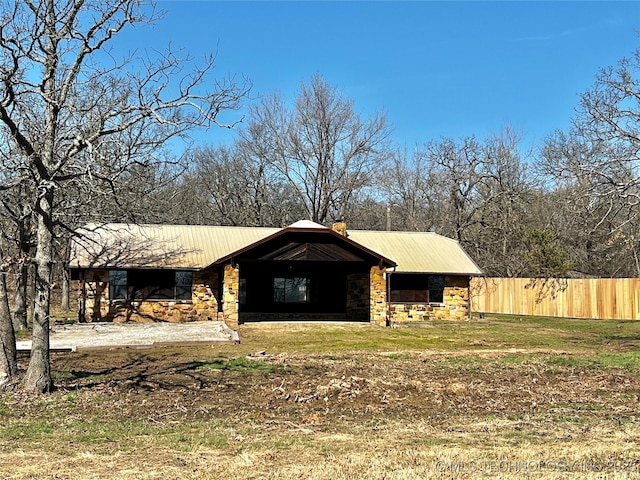 exterior space featuring metal roof, stone siding, a chimney, and fence