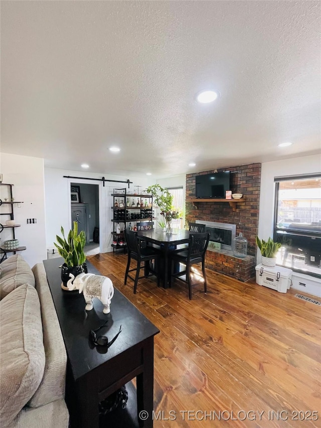 living room featuring a textured ceiling, a barn door, recessed lighting, a fireplace, and wood finished floors