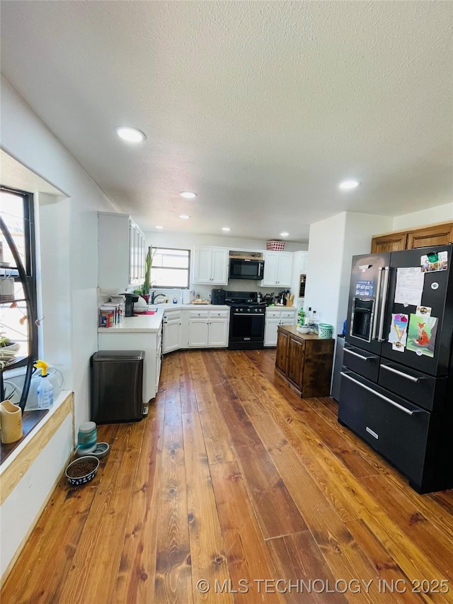 kitchen featuring white cabinets, wood-type flooring, light countertops, a textured ceiling, and black appliances