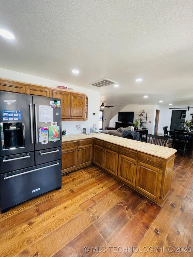 kitchen with light countertops, wood-type flooring, a peninsula, and stainless steel fridge with ice dispenser