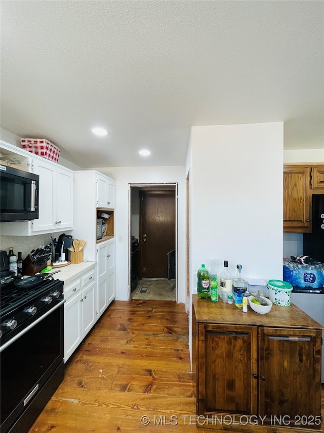 kitchen with recessed lighting, light countertops, white cabinets, wood finished floors, and black appliances