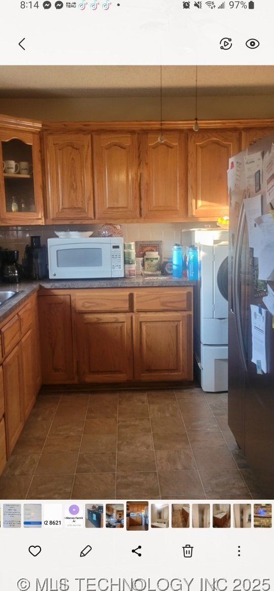 103877 US Highway 59 N, Sallisaw, OK 74955 - kitchen with white microwave, freestanding refrigerator, washer / clothes dryer, glass insert cabinets, and brown cabinetry