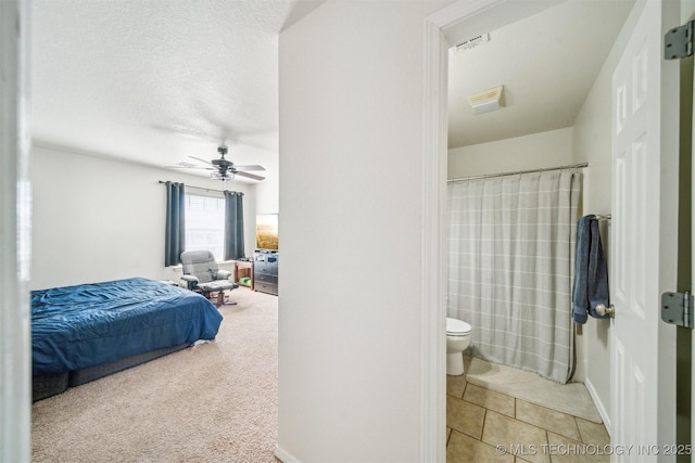 bedroom with light tile patterned floors, light colored carpet, ensuite bathroom, a ceiling fan, and a textured ceiling