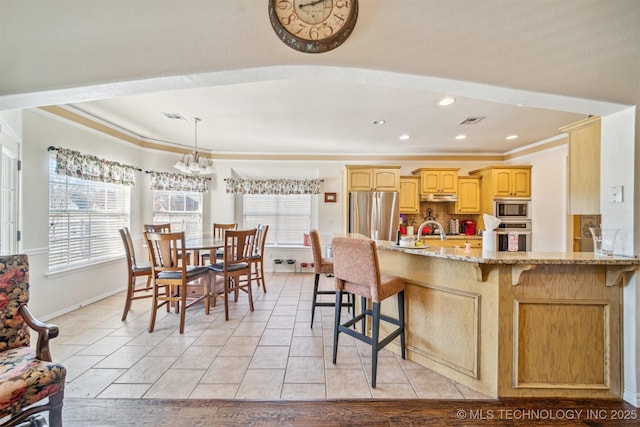 kitchen with stainless steel appliances, a chandelier, a kitchen breakfast bar, and light stone countertops