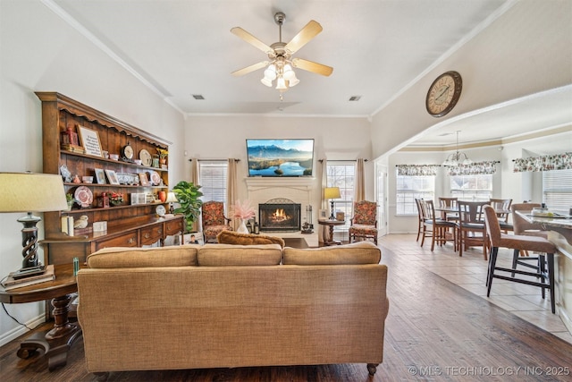 living room featuring a ceiling fan, a fireplace, visible vents, and crown molding