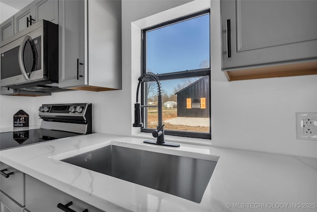 kitchen featuring stainless steel appliances, gray cabinets, a sink, and light stone counters