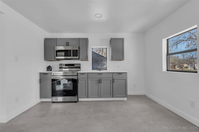 kitchen featuring baseboards, appliances with stainless steel finishes, gray cabinets, and concrete flooring