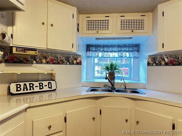 kitchen with light countertops, a sink, a textured ceiling, and white cabinetry