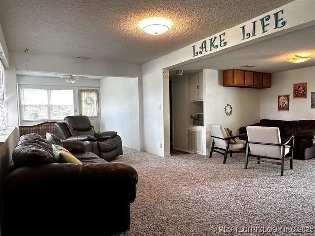 carpeted living area with a textured ceiling, visible vents, and a ceiling fan