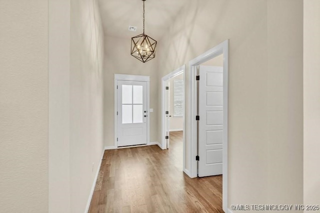 doorway to outside featuring baseboards, wood finished floors, and an inviting chandelier