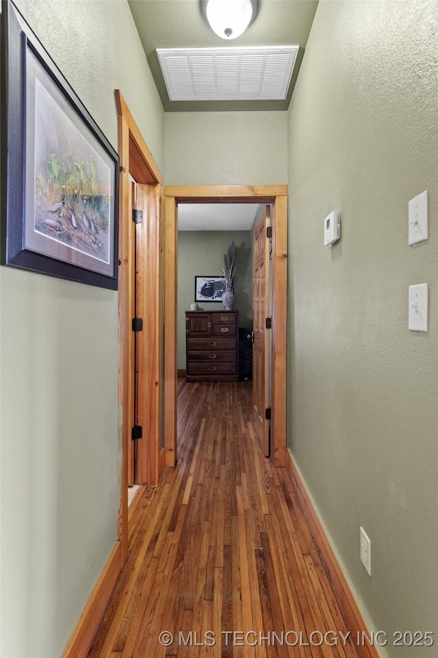 corridor with hardwood / wood-style flooring, visible vents, and baseboards