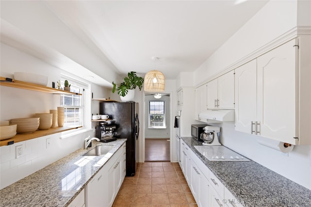 kitchen featuring stainless steel microwave, under cabinet range hood, white cabinetry, open shelves, and a sink