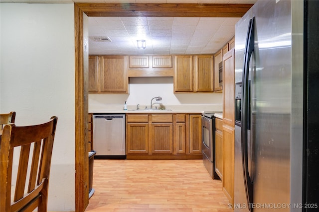 kitchen featuring light countertops, appliances with stainless steel finishes, light wood-style floors, brown cabinetry, and a sink