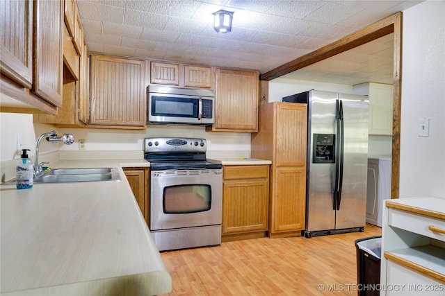 kitchen with washer / dryer, light wood-style flooring, stainless steel appliances, light countertops, and a sink