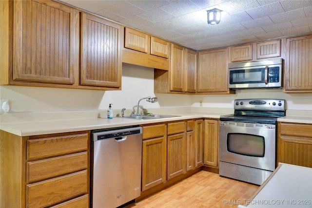 kitchen featuring appliances with stainless steel finishes, light wood-style floors, light countertops, and a sink