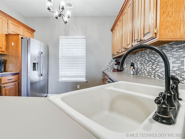 kitchen with a sink, visible vents, light countertops, stainless steel fridge with ice dispenser, and tasteful backsplash