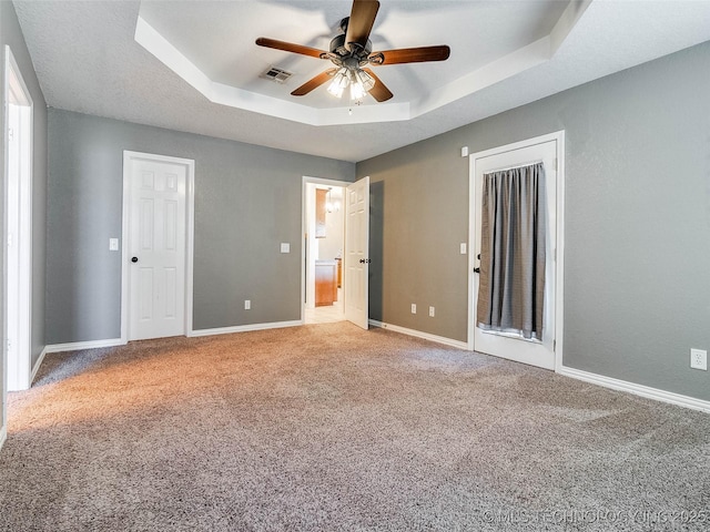 unfurnished bedroom featuring ceiling fan, visible vents, baseboards, a tray ceiling, and carpet