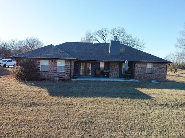 rear view of house featuring roof with shingles, a chimney, a lawn, and brick siding