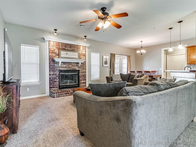 living room with baseboards, visible vents, carpet floors, a brick fireplace, and ceiling fan with notable chandelier