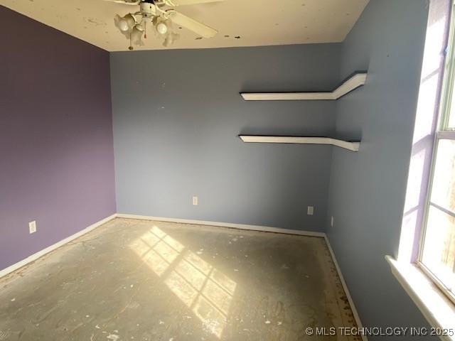 spare room featuring ceiling fan, concrete floors, and baseboards