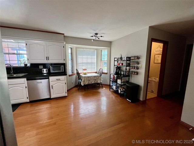 kitchen with dark countertops, white cabinets, a sink, light wood-type flooring, and dishwasher