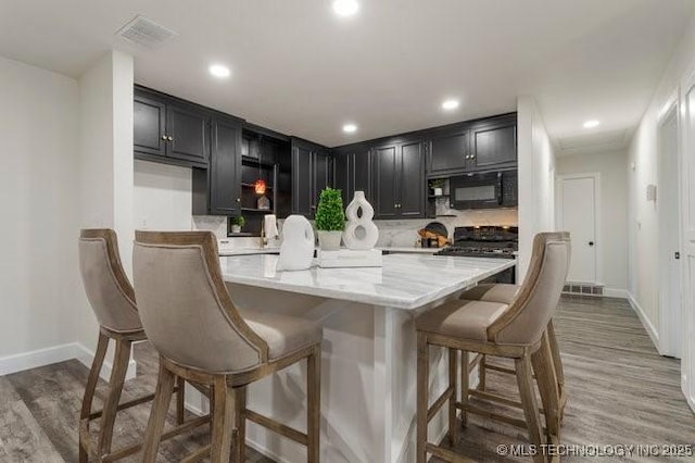 kitchen with light wood-type flooring, a kitchen bar, black microwave, and dark cabinets