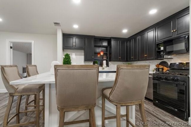 kitchen featuring dark cabinets, visible vents, black appliances, and wood finished floors