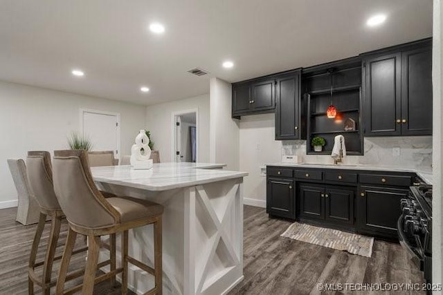 kitchen featuring decorative backsplash, dark wood-type flooring, gas stove, a sink, and dark cabinets