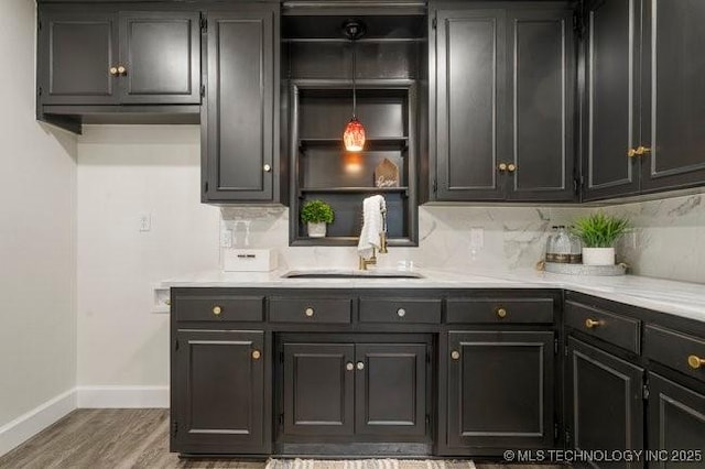 kitchen featuring wood finished floors, a sink, baseboards, light countertops, and tasteful backsplash