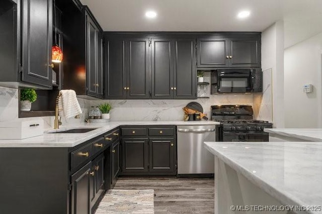 kitchen with tasteful backsplash, light wood-style floors, dark cabinetry, black appliances, and a sink