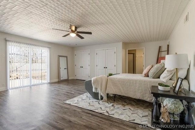 bedroom featuring wood finished floors, a ceiling fan, baseboards, visible vents, and multiple closets