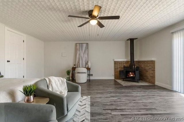 living room with a wood stove, wood finished floors, a ceiling fan, and baseboards