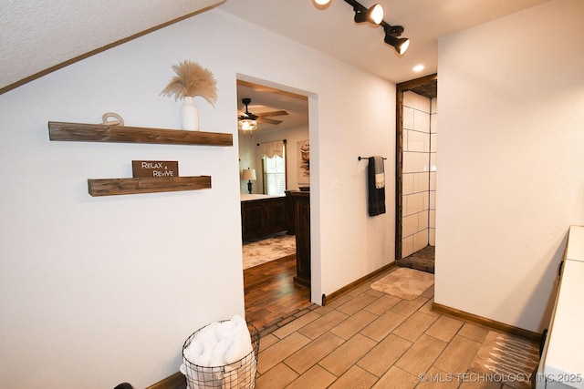 hallway with light wood finished floors, baseboards, and vaulted ceiling