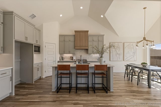 kitchen featuring a center island with sink, light countertops, stainless steel microwave, visible vents, and gray cabinetry