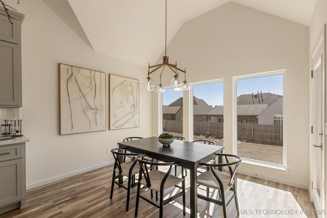 dining area featuring a chandelier, high vaulted ceiling, light wood-style flooring, and baseboards