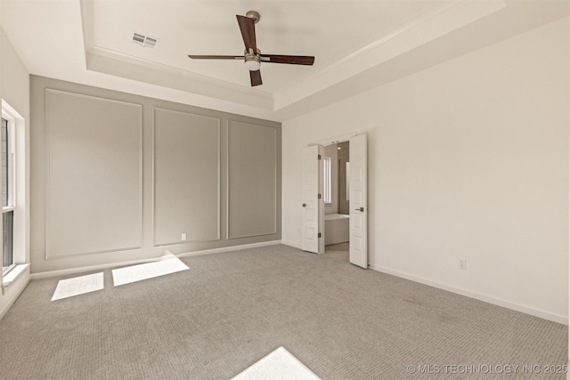 unfurnished bedroom with visible vents, a raised ceiling, connected bathroom, baseboards, and carpet